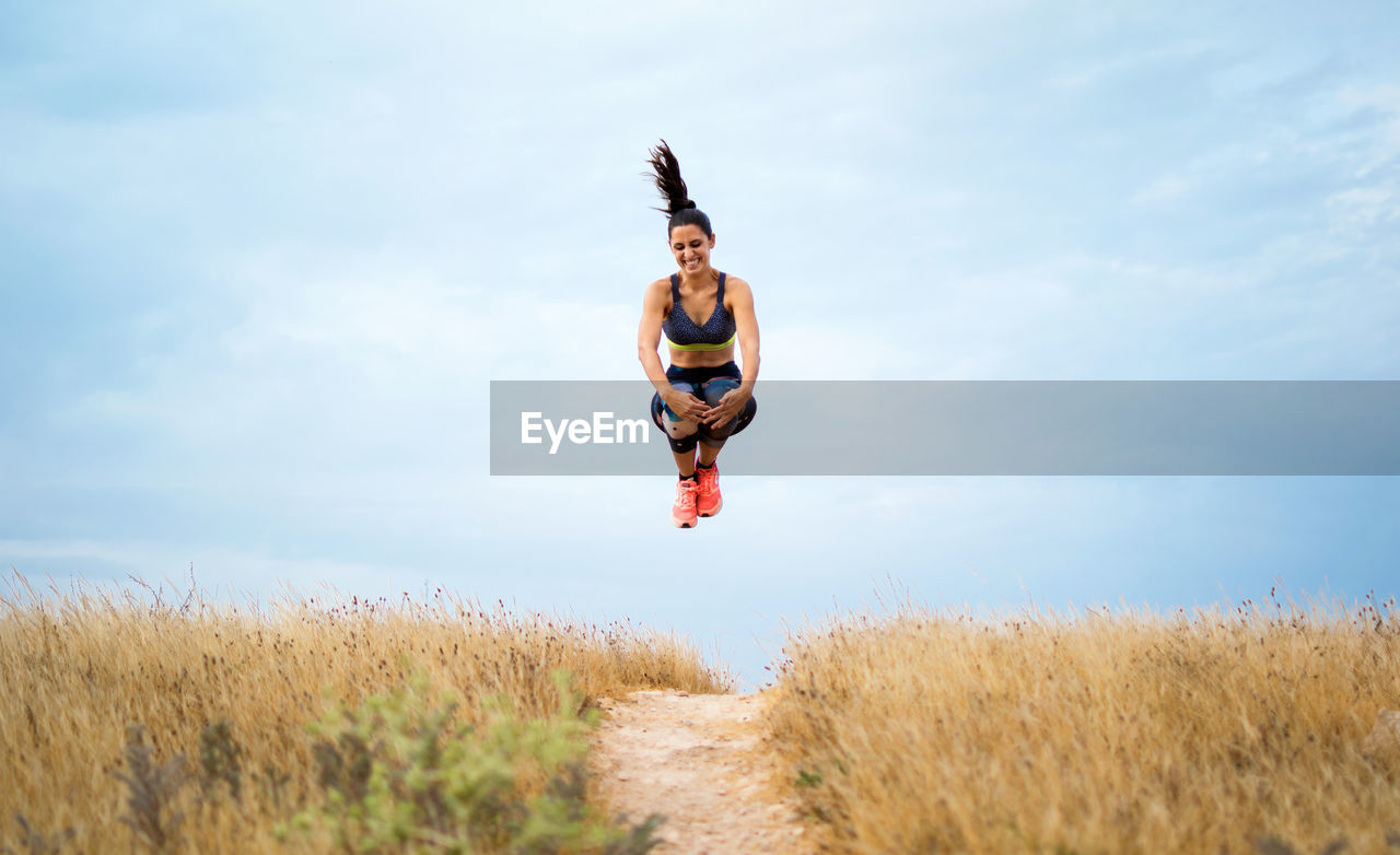 Full length of young woman jumping on grassy land