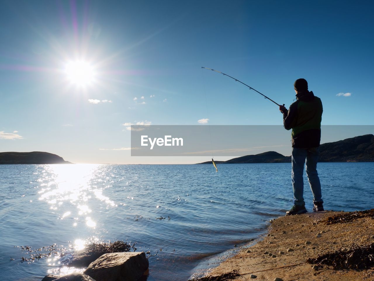 Active man is fishing on sea from rock. man throw lure into peacefull water. fisherman silhouette 