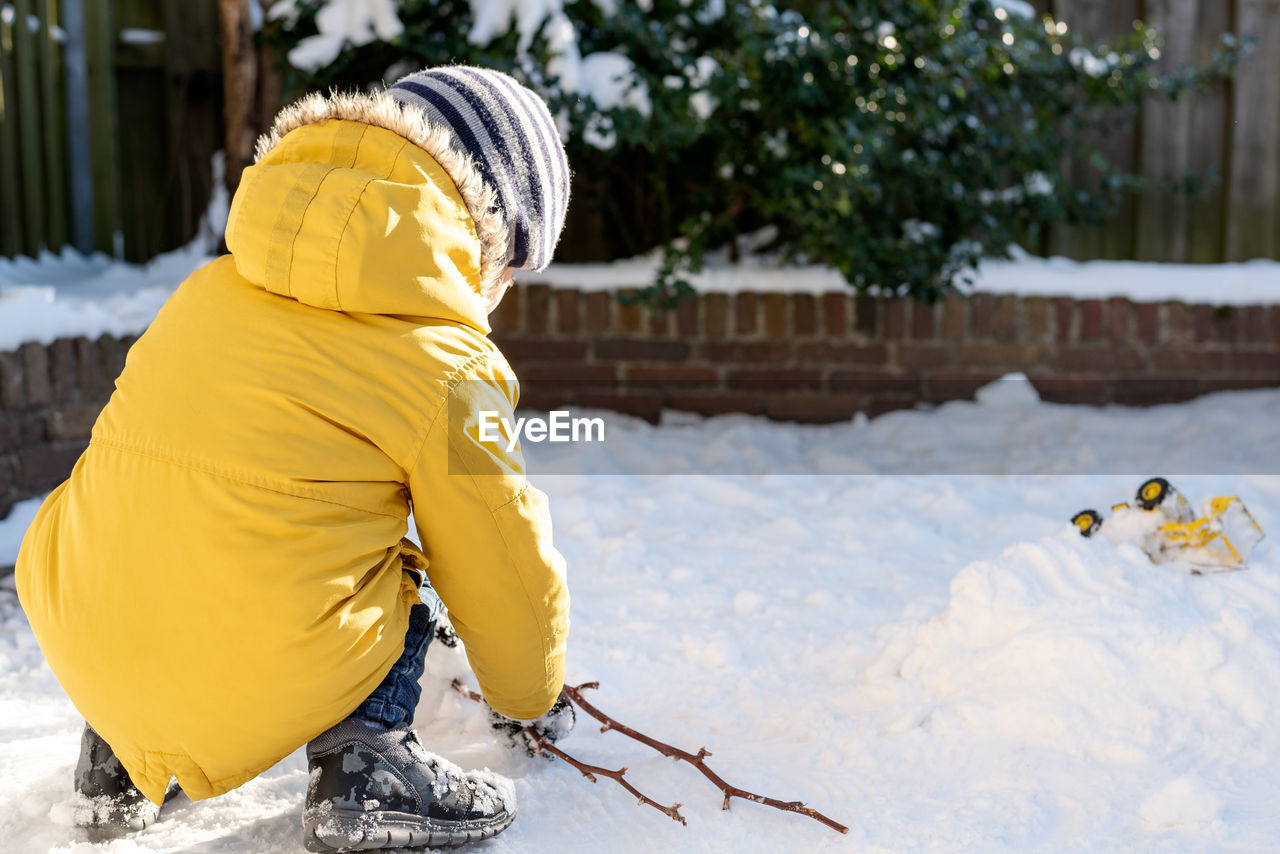 Little boy plays with snow in the backyard.