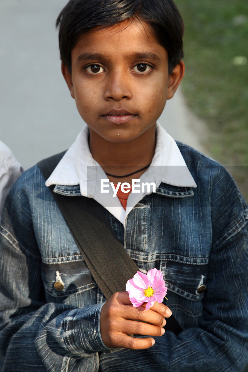 PORTRAIT OF BOY HOLDING FLOWER WHILE STANDING BY PLANT