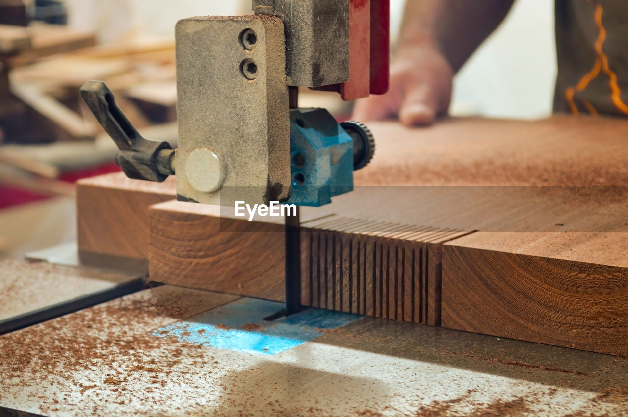 A man cuts wood on a circular saw in a joinery, band saw, holding a plank