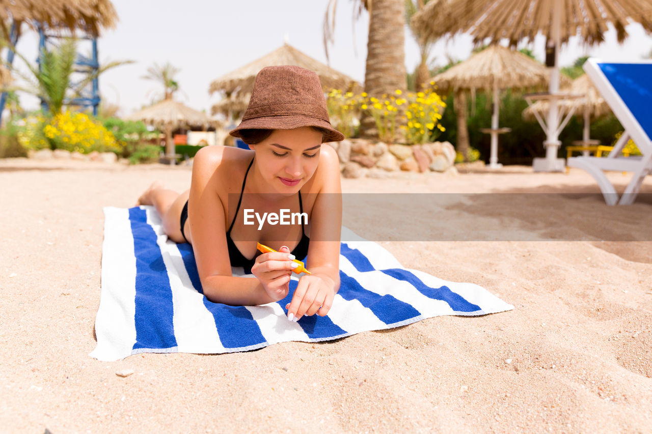 Happy woman applying sunscreen while lying on towel at beach