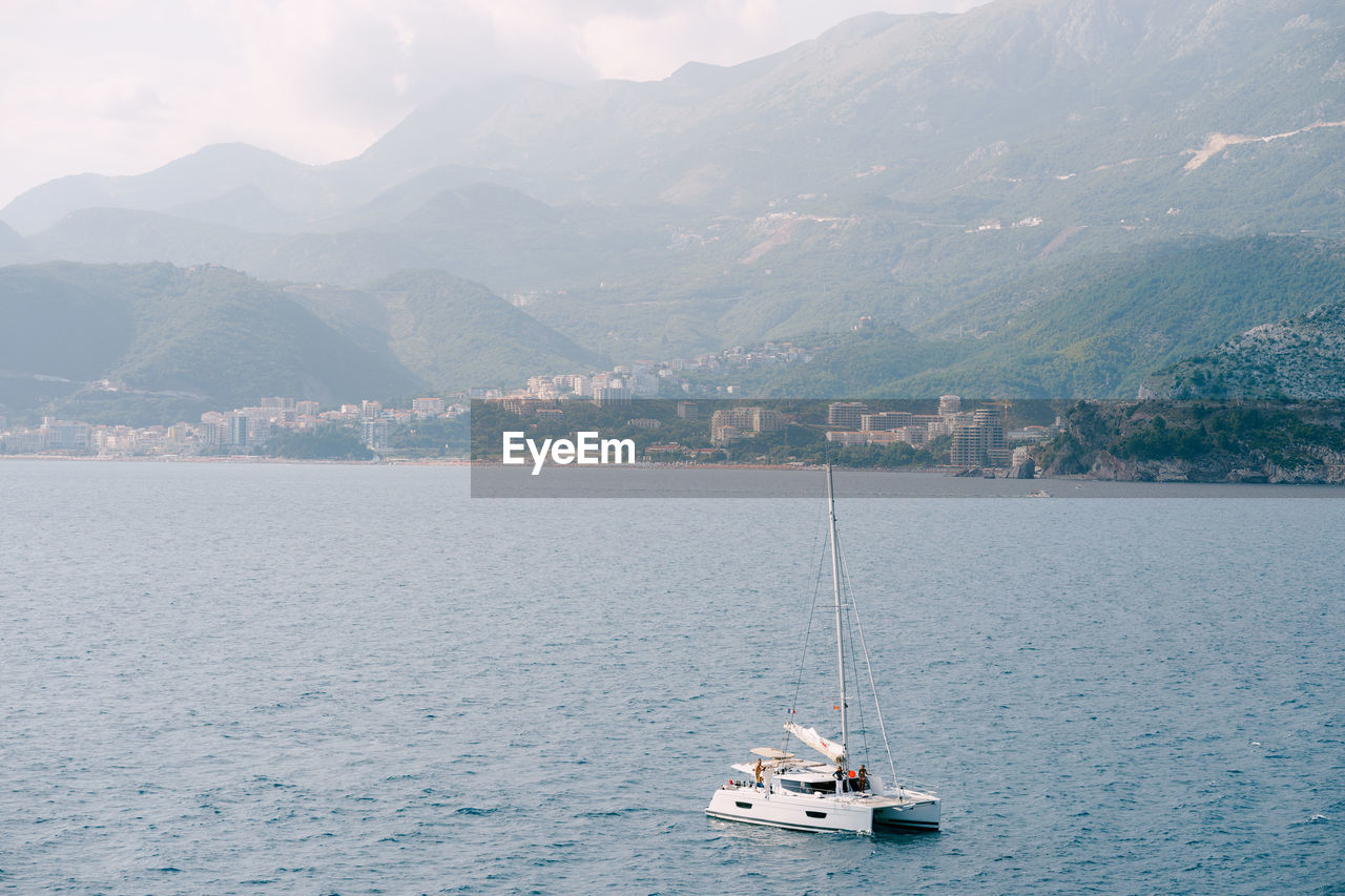 SAILBOAT SAILING ON SEA AGAINST MOUNTAINS