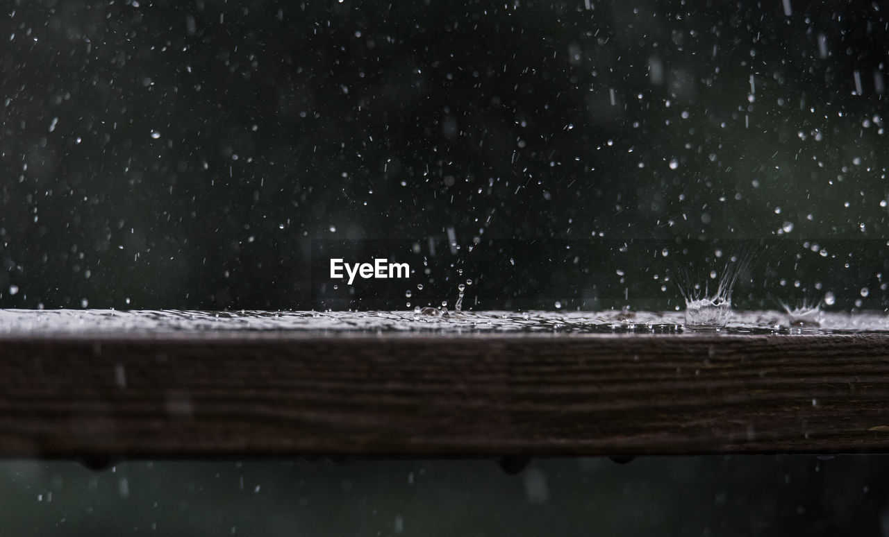 Close up of raindrops hitting a wooden railing with a splash.
