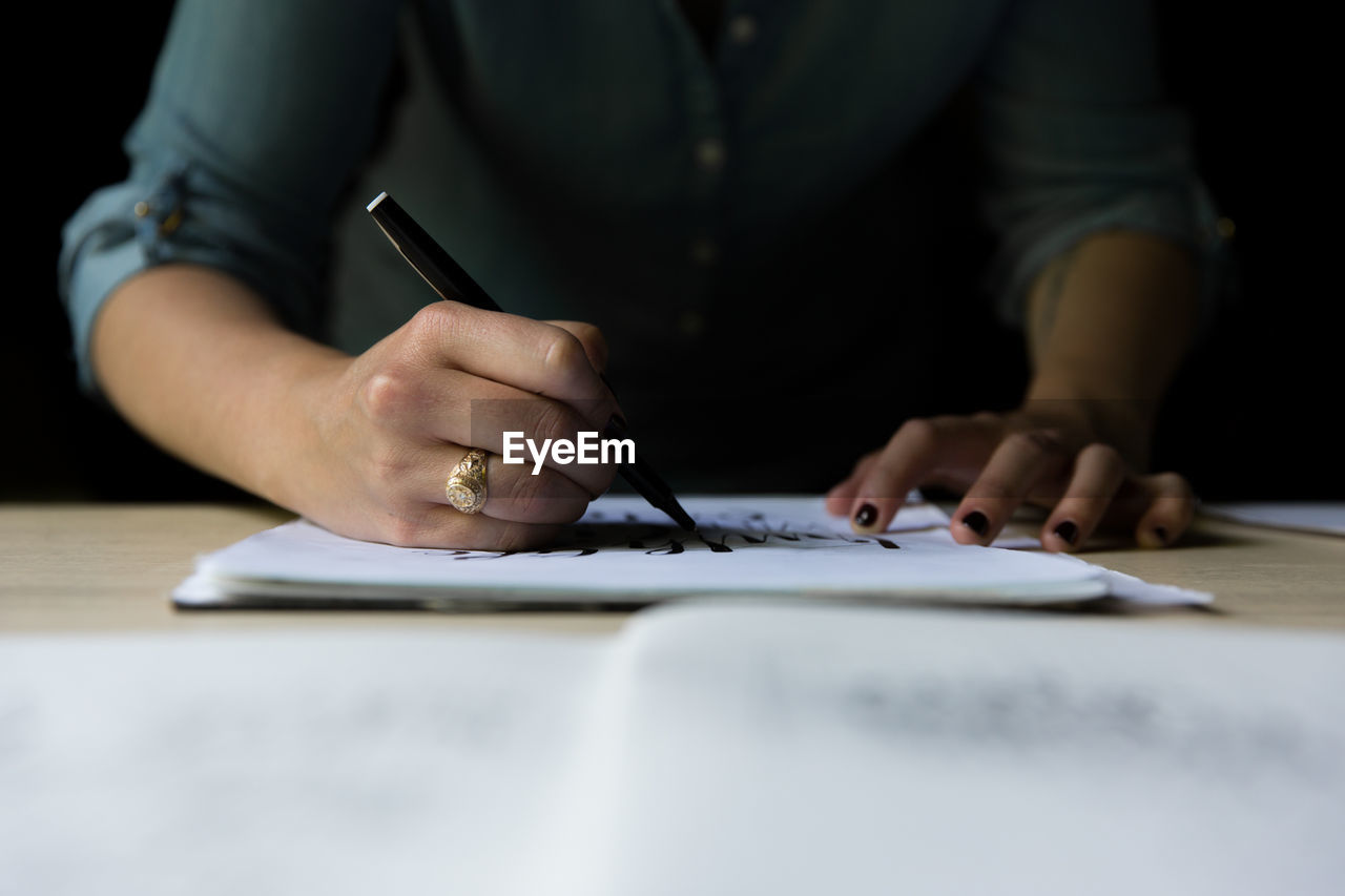 Midsection of woman writing on paper at table