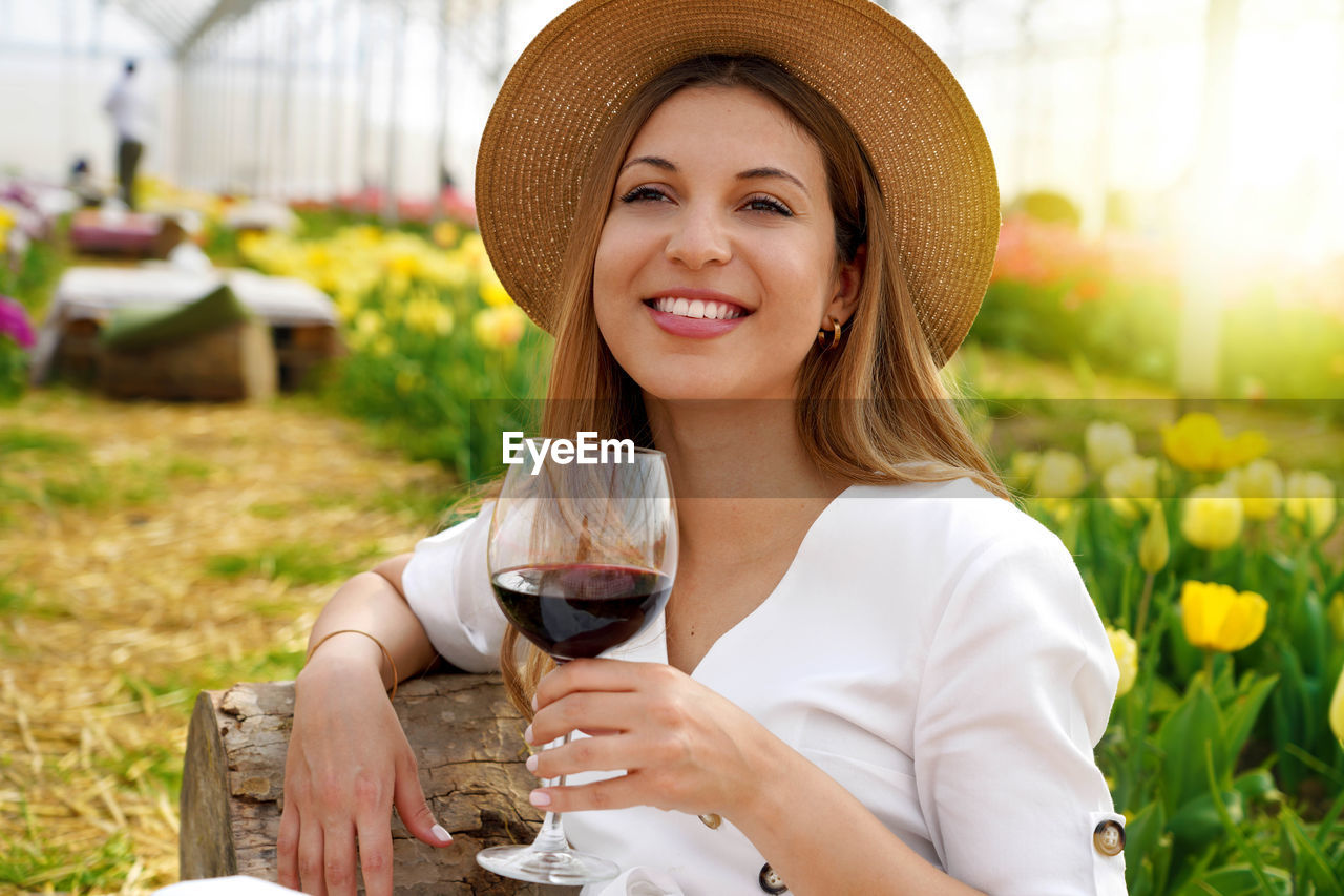 Relaxed beautiful woman enjoying a glass of red wine between tulips on spring time