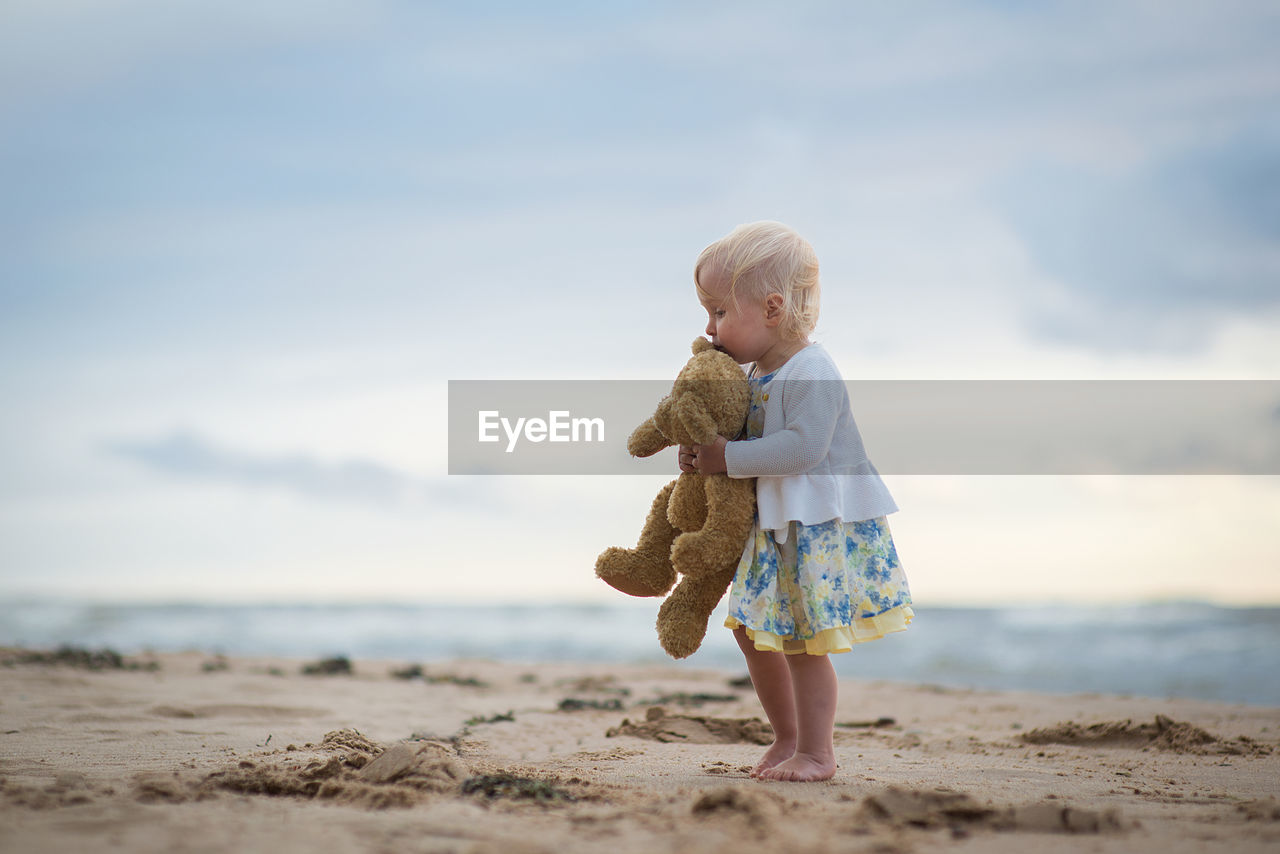 Girl with stuffed toy at beach against sky