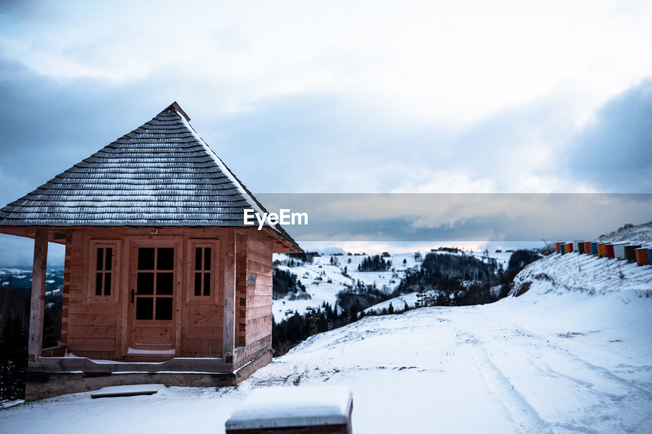 snow, winter, architecture, cold temperature, built structure, building exterior, building, house, landscape, sky, nature, cloud, scenics - nature, environment, beauty in nature, mountain, hut, no people, residential district, wood, rural scene, mountain range, travel destinations, log cabin, outdoors, white, non-urban scene, day, land, travel, tranquility, tranquil scene, holiday