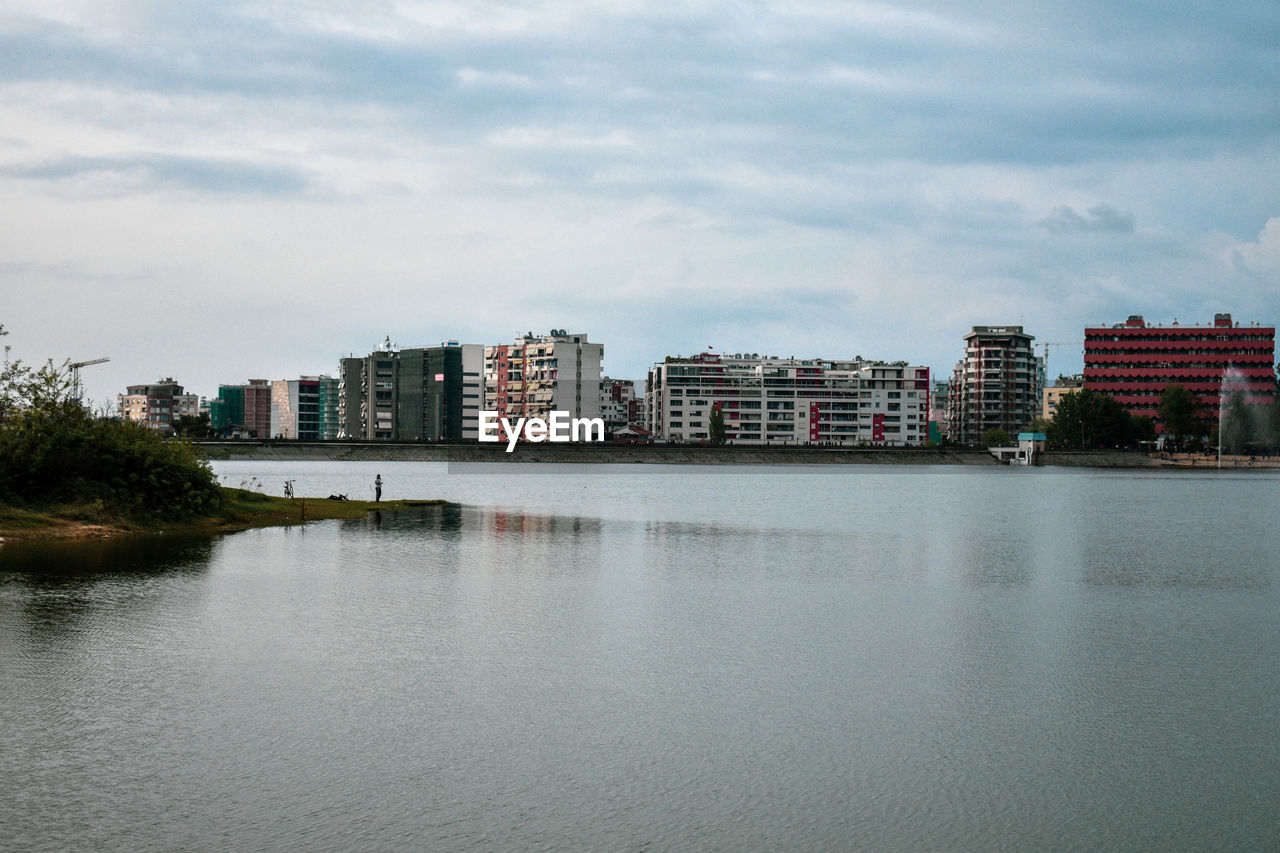 Buildings by river against sky in city