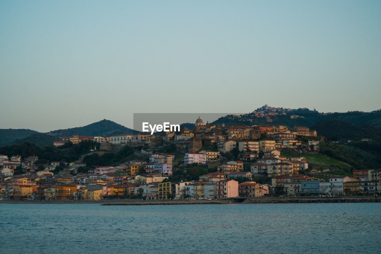 Houses on mountain by sea against clear sky during sunset