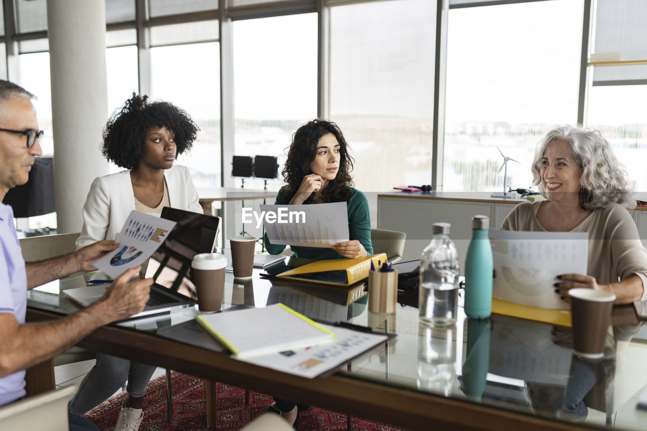 Happy senior businesswoman sitting with coworkers in office