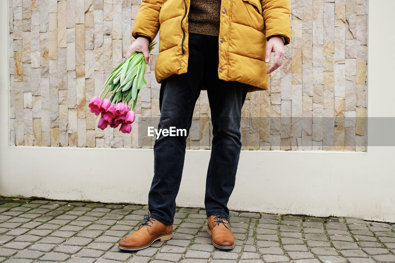 Blond man in a yellow winter jacket with a bouquet of tulips in hands