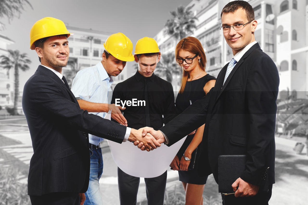 Businessman and architect shaking hands by colleagues at construction site