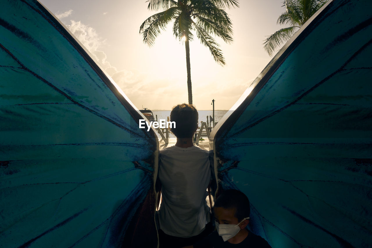 Rear view of woman and boy standing by palm trees against sky