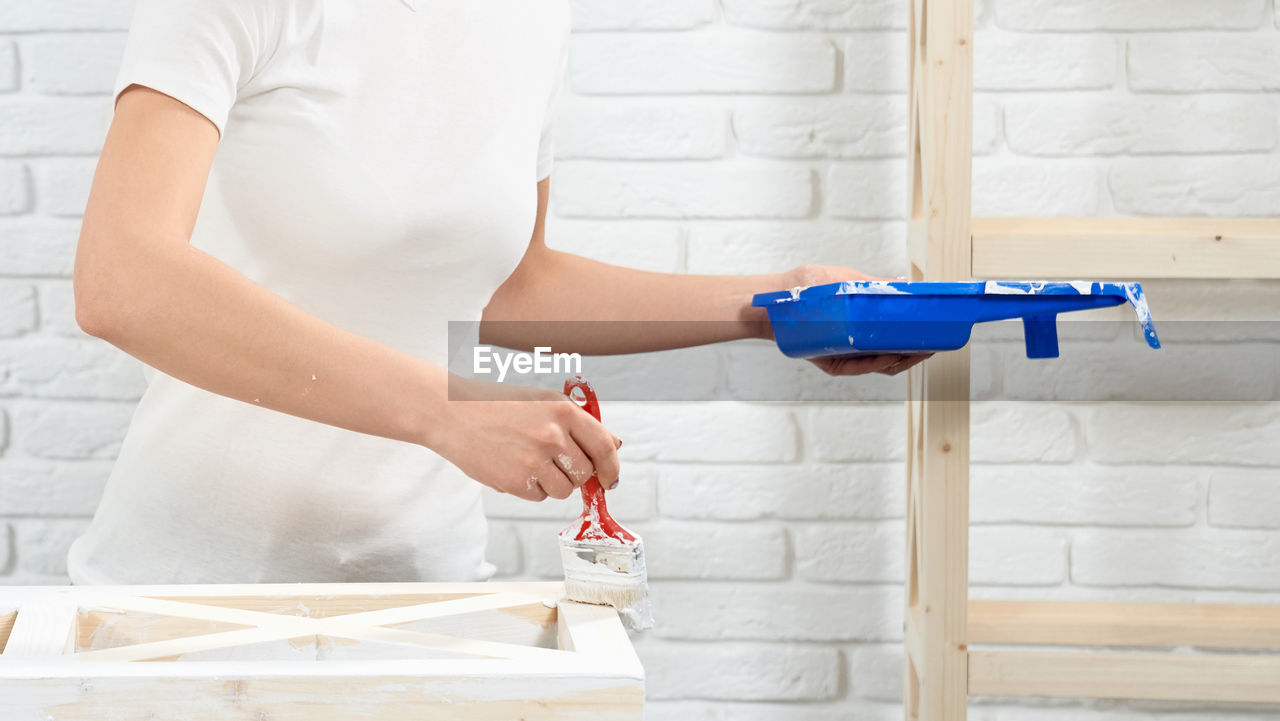 MIDSECTION OF WOMAN STANDING AGAINST WHITE WALL