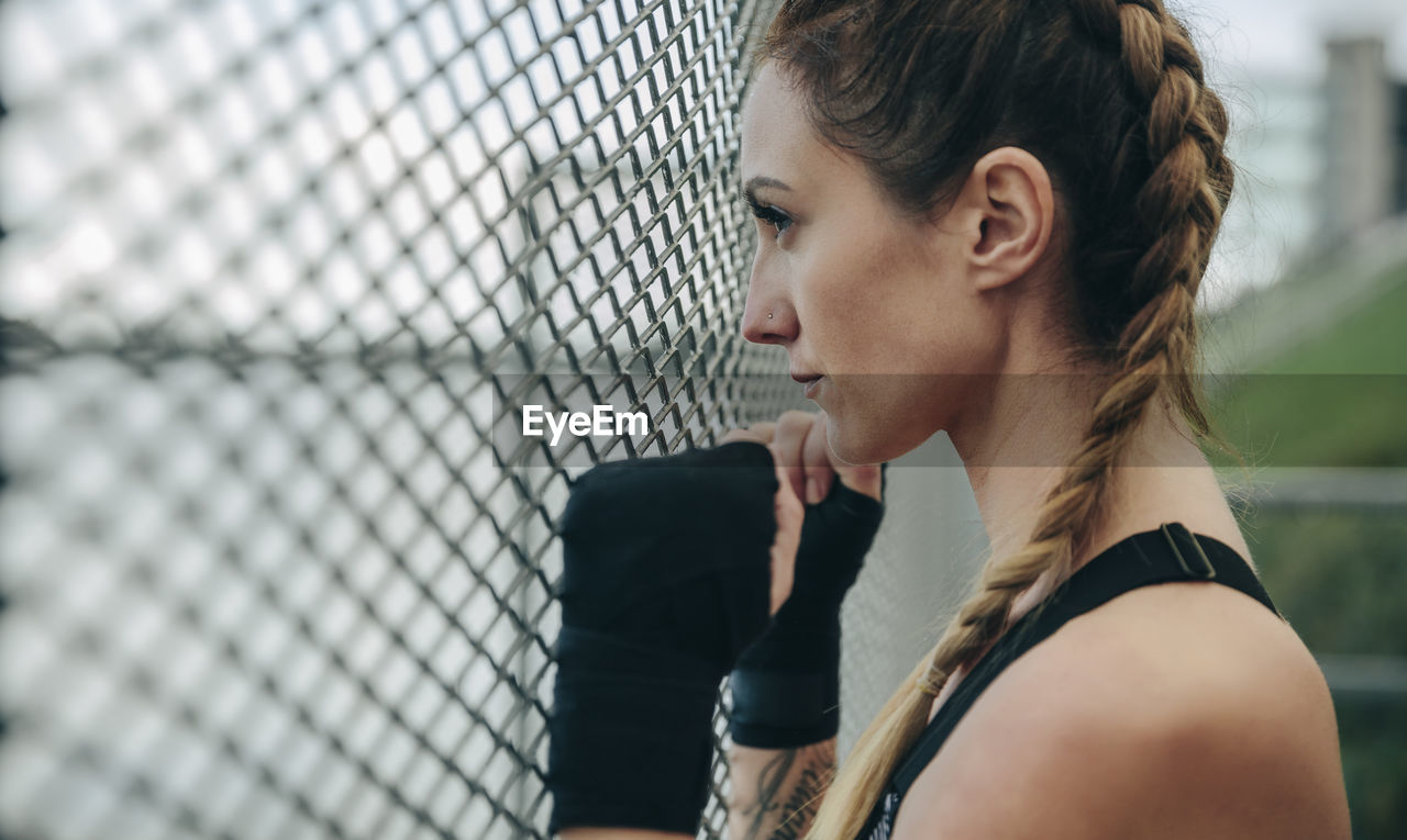 Woman looking away while standing by chainlink fence