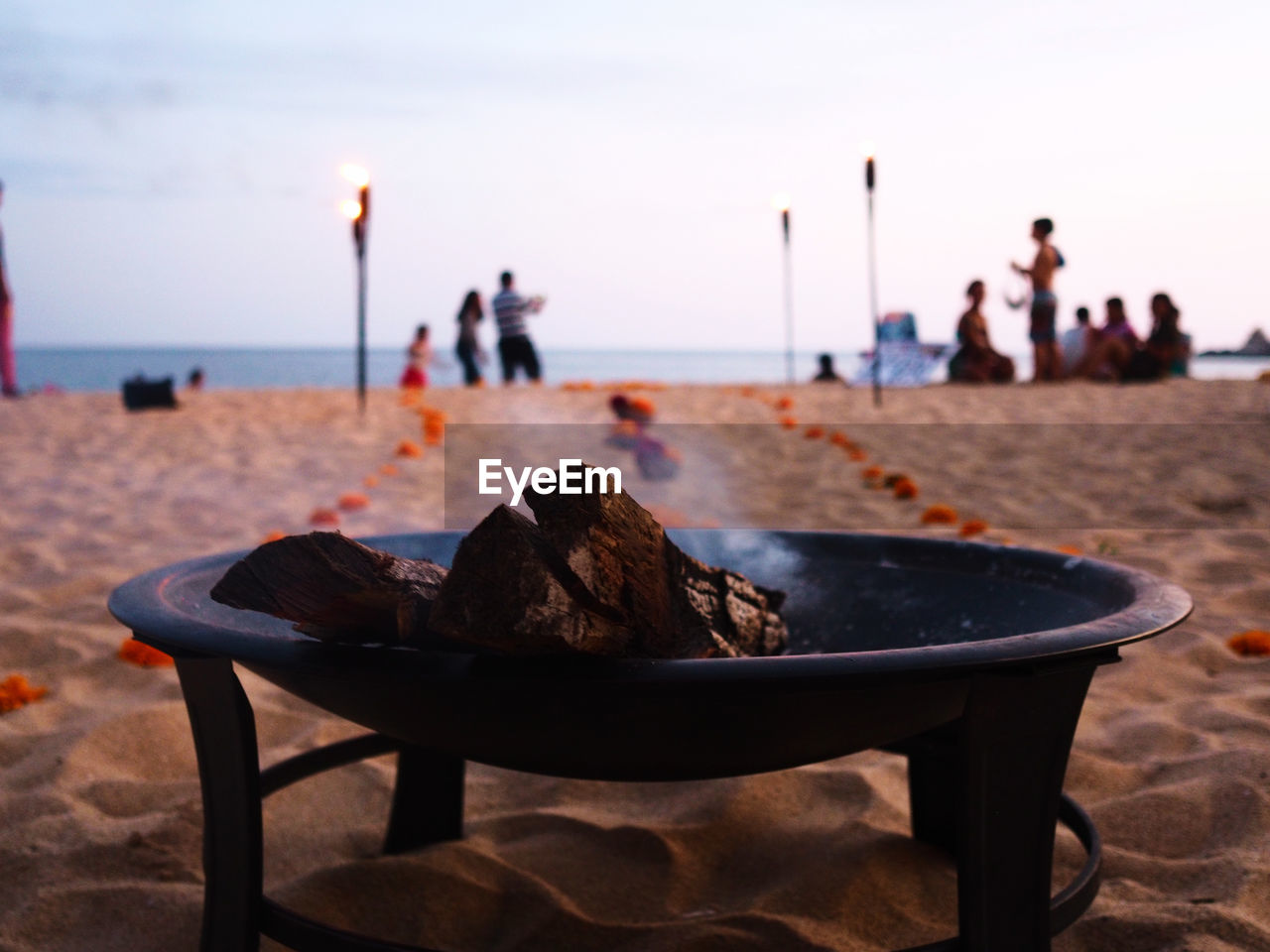 Close-up of fire pit on beach against sky during sunset