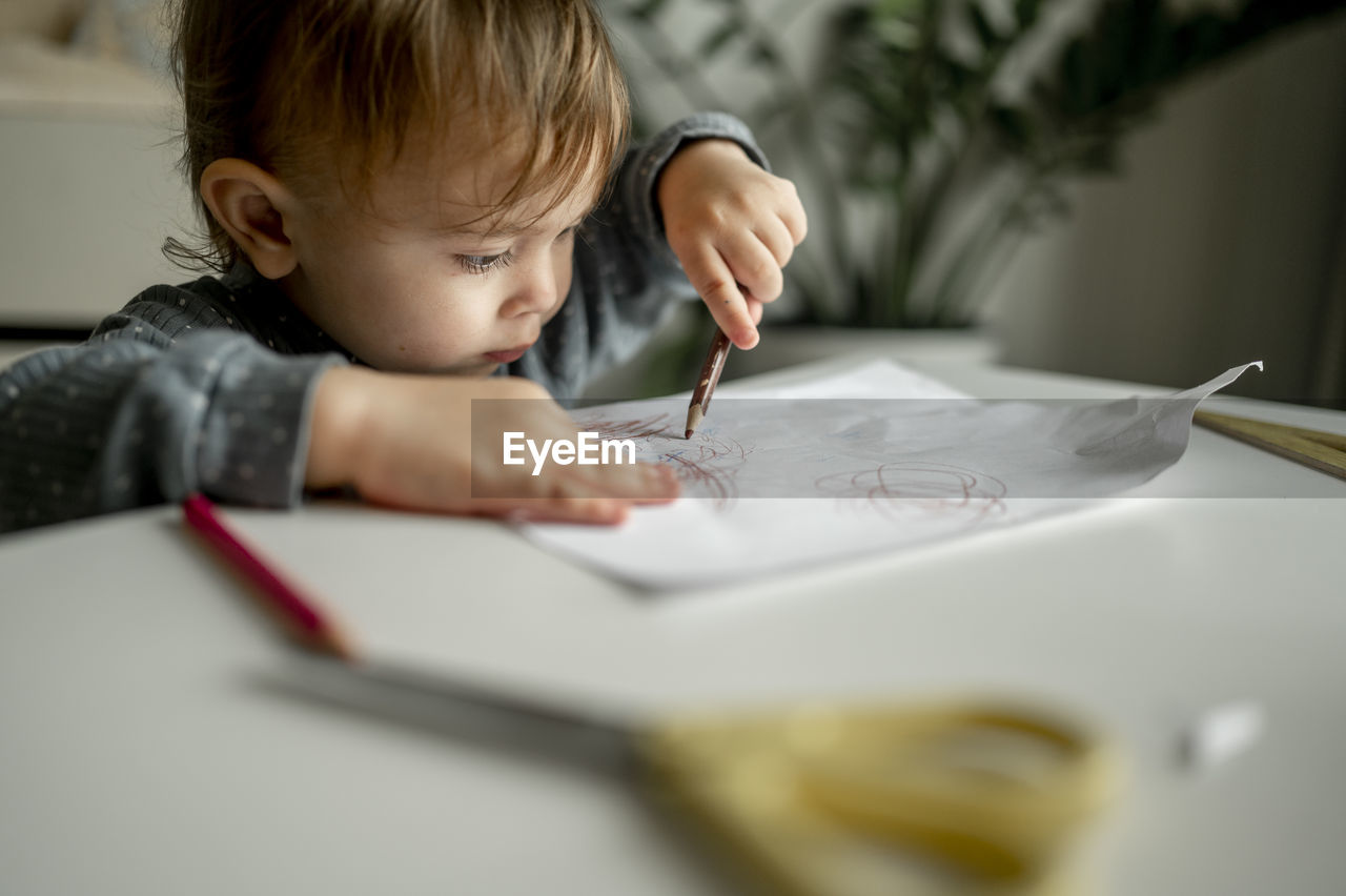 Boy drawing on paper with colored pencil at home