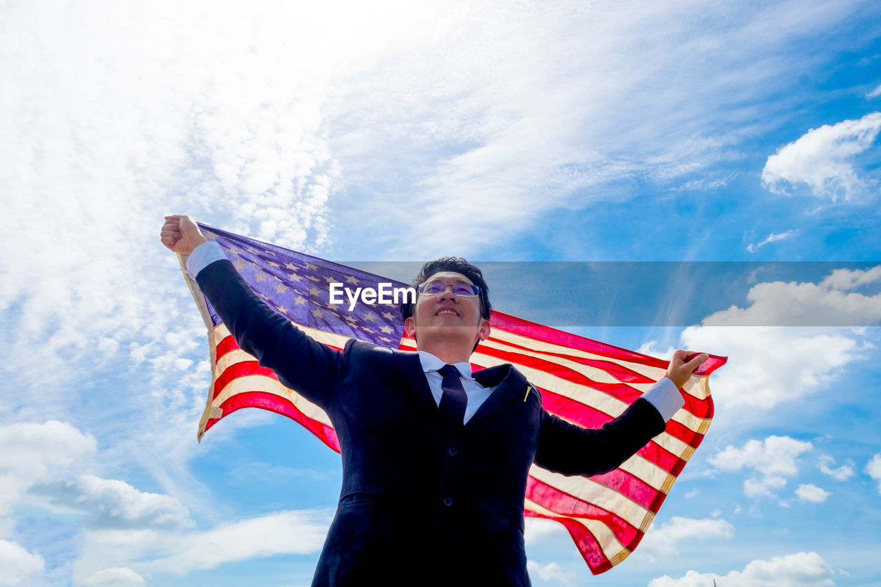 Low angle view of businessman holding american flag against sky