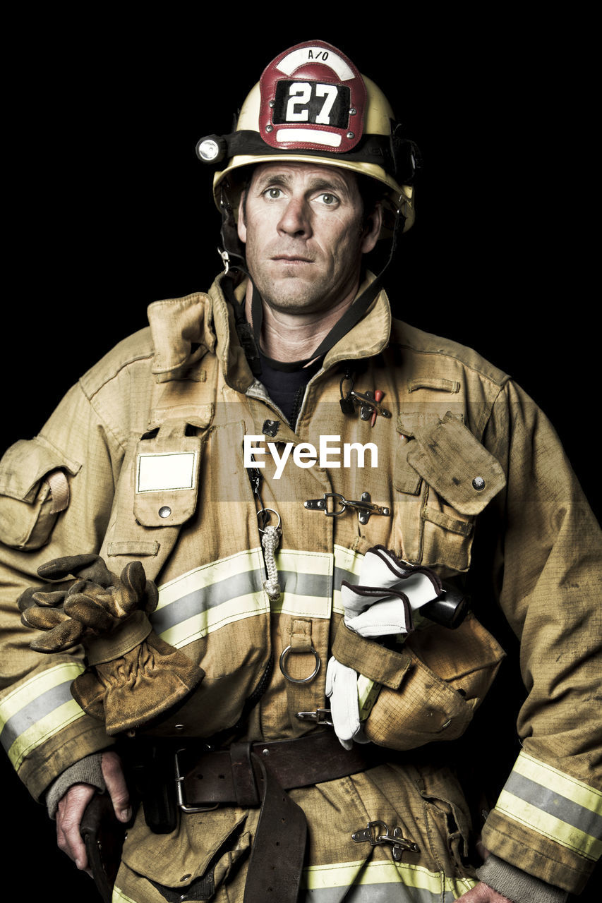 Portrait of firefighter standing against black background