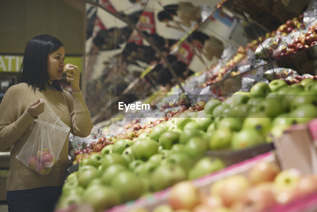 View of woman standing in supermarkets and choosing apples