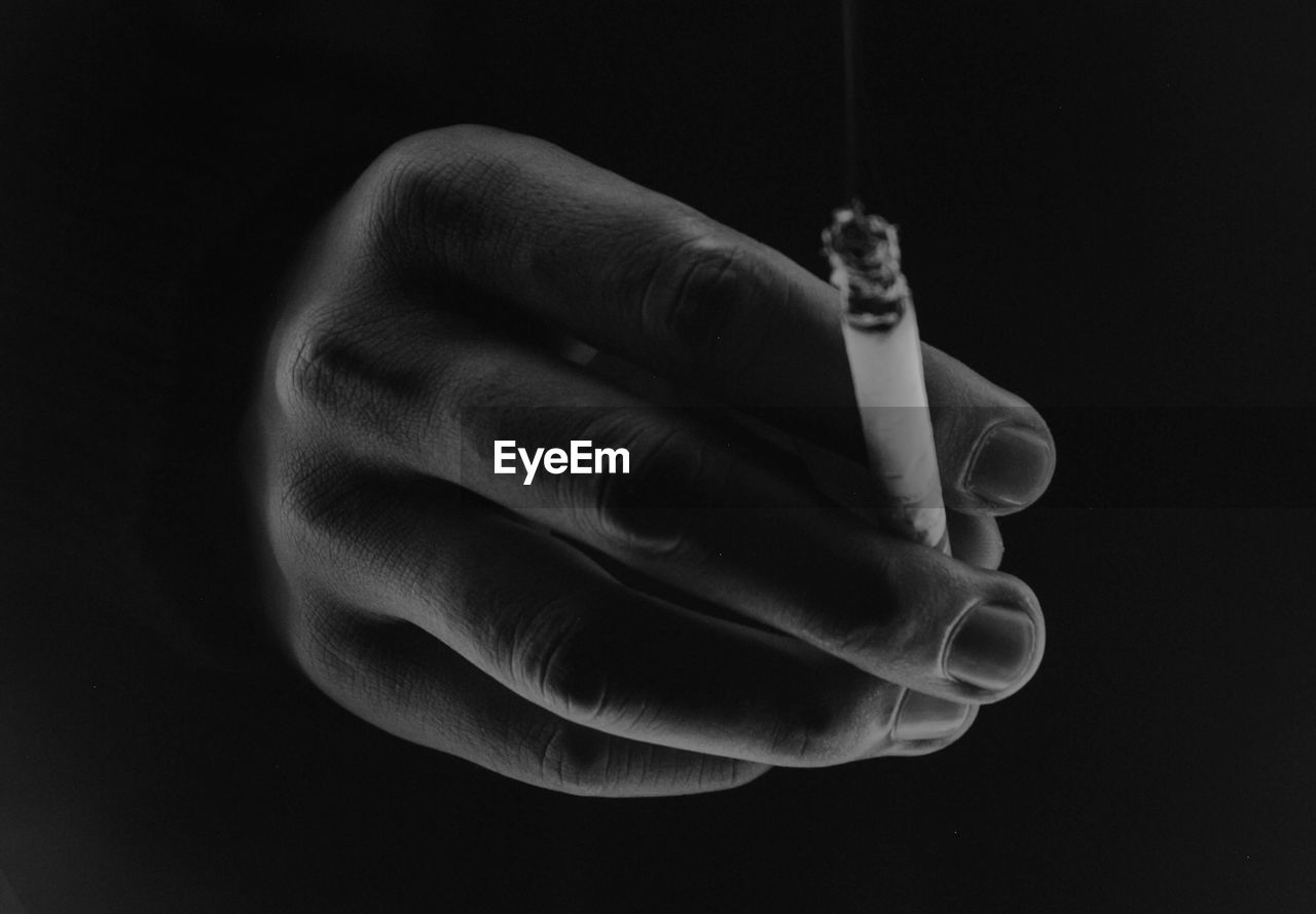 Close-up of hand holding cigarette against black background