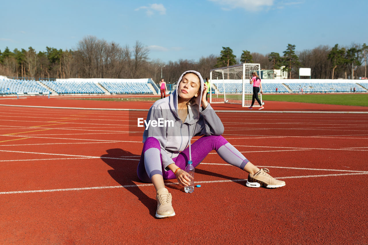 Full length of woman wearing hoodie sitting on running track