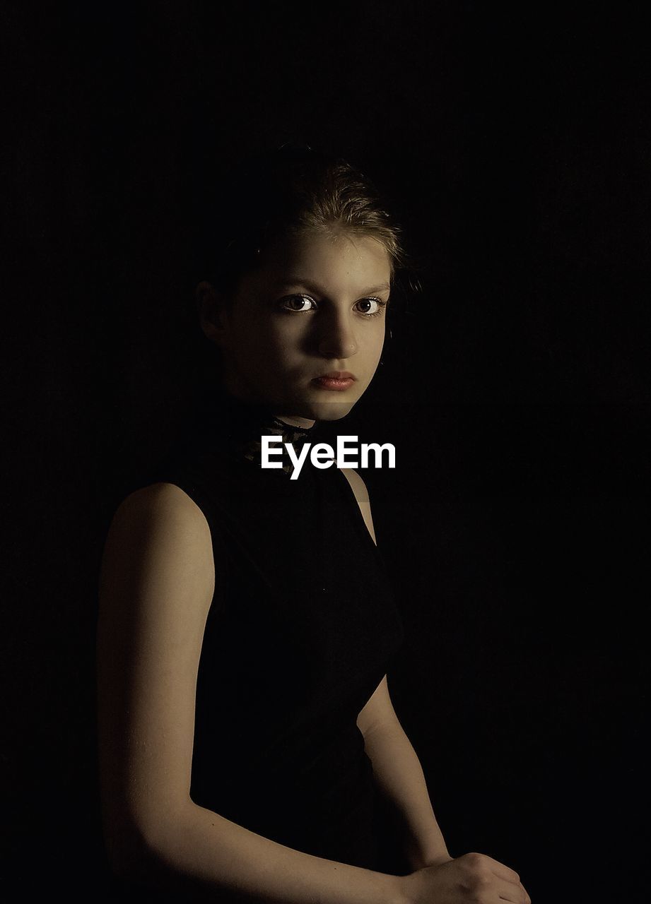 Portrait of girl sitting against black background