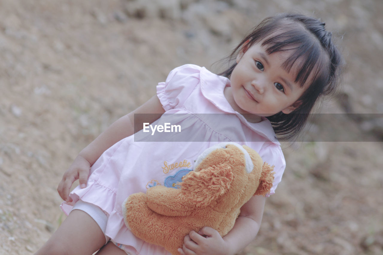 Portrait of cute smiling baby girl holding stuffed toy outdoors