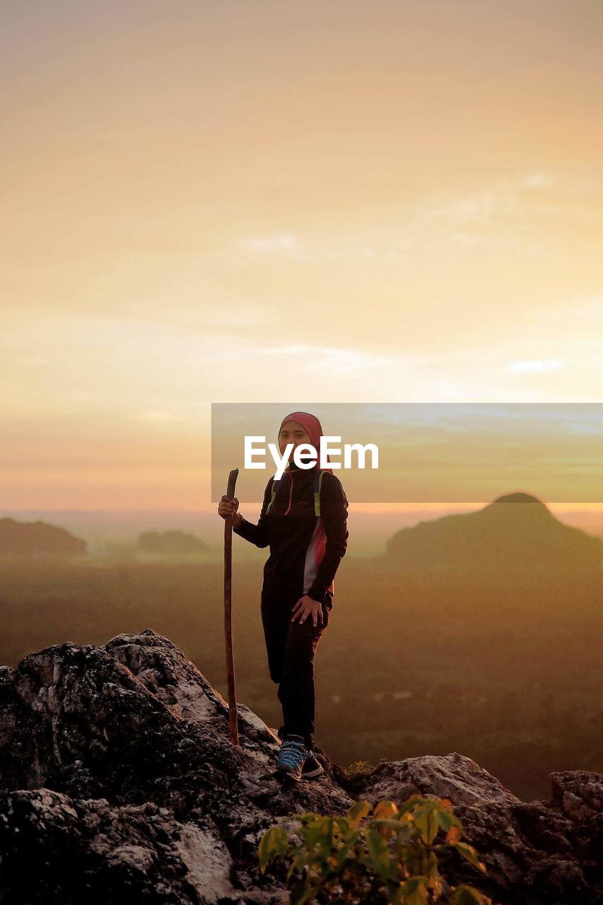 Portrait of woman standing on rock against sky during sunset