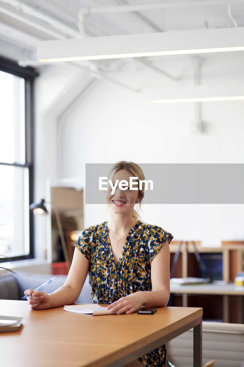 Portrait of smiling businesswoman sitting at table in office