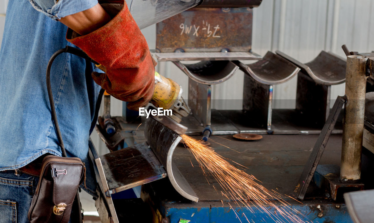 Midsection of manual worker working on metal structure in factory