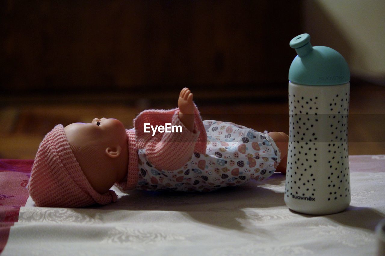 Close-up of toy baby by bottle on bed