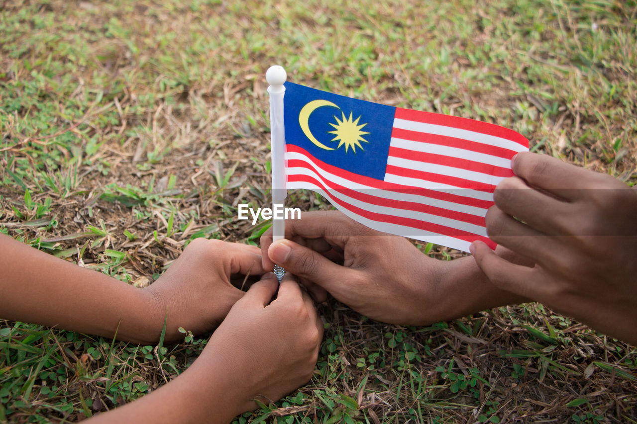 Cropped hands of friends holding malaysian flag on grassy field