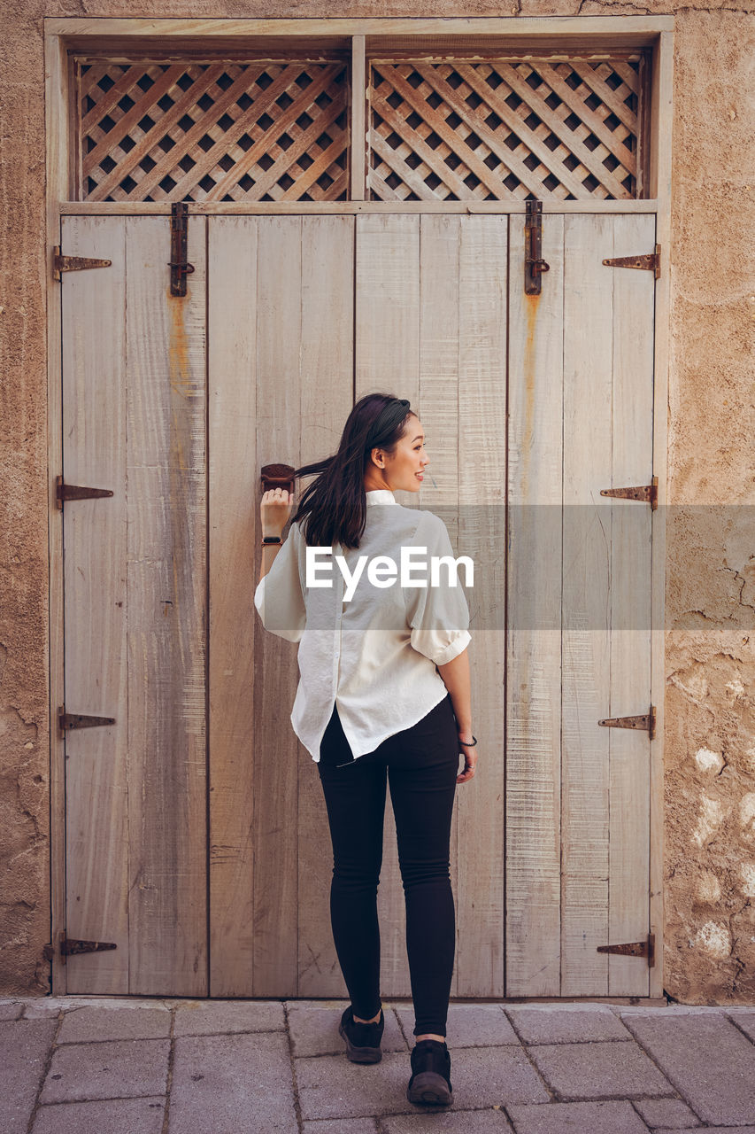 Back view of female traveler in casual wear while open the door during sightseeing tour in al fahidi historical neighbourhood in dubai