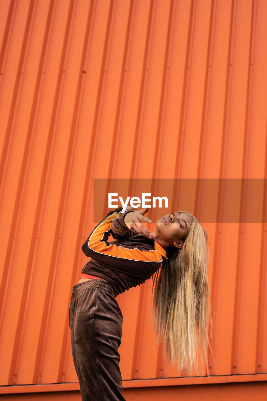 Cheerful african american woman in sportswear dancing in the street on an orange background