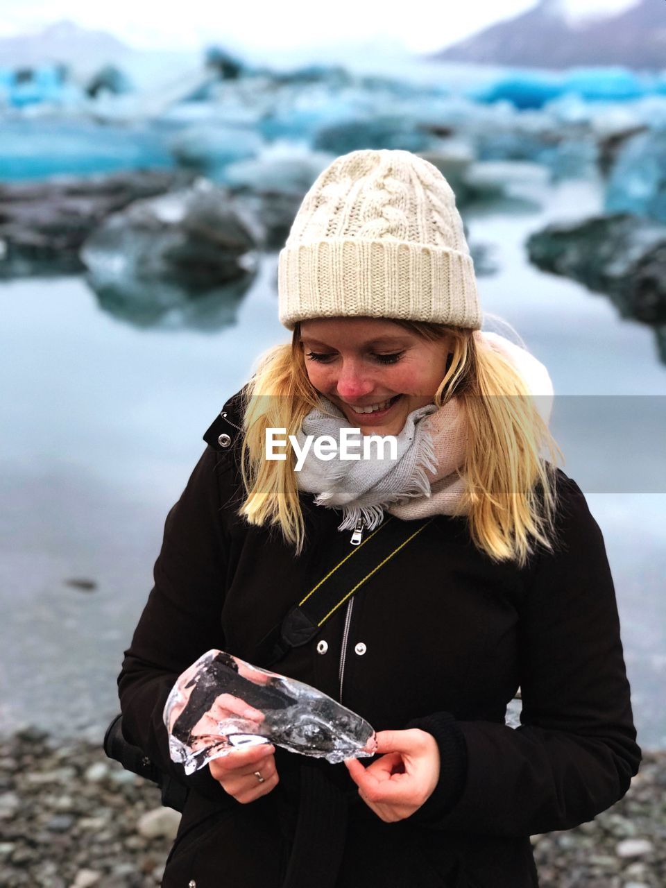 Smiling young woman holding ice while standing against glaciers