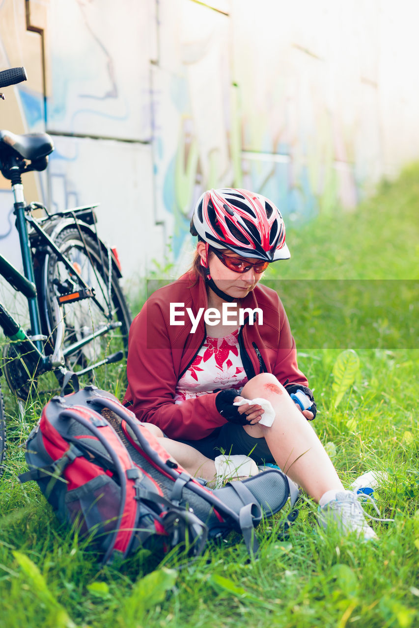 Injured female cyclist applying medicine on wound while sitting at park