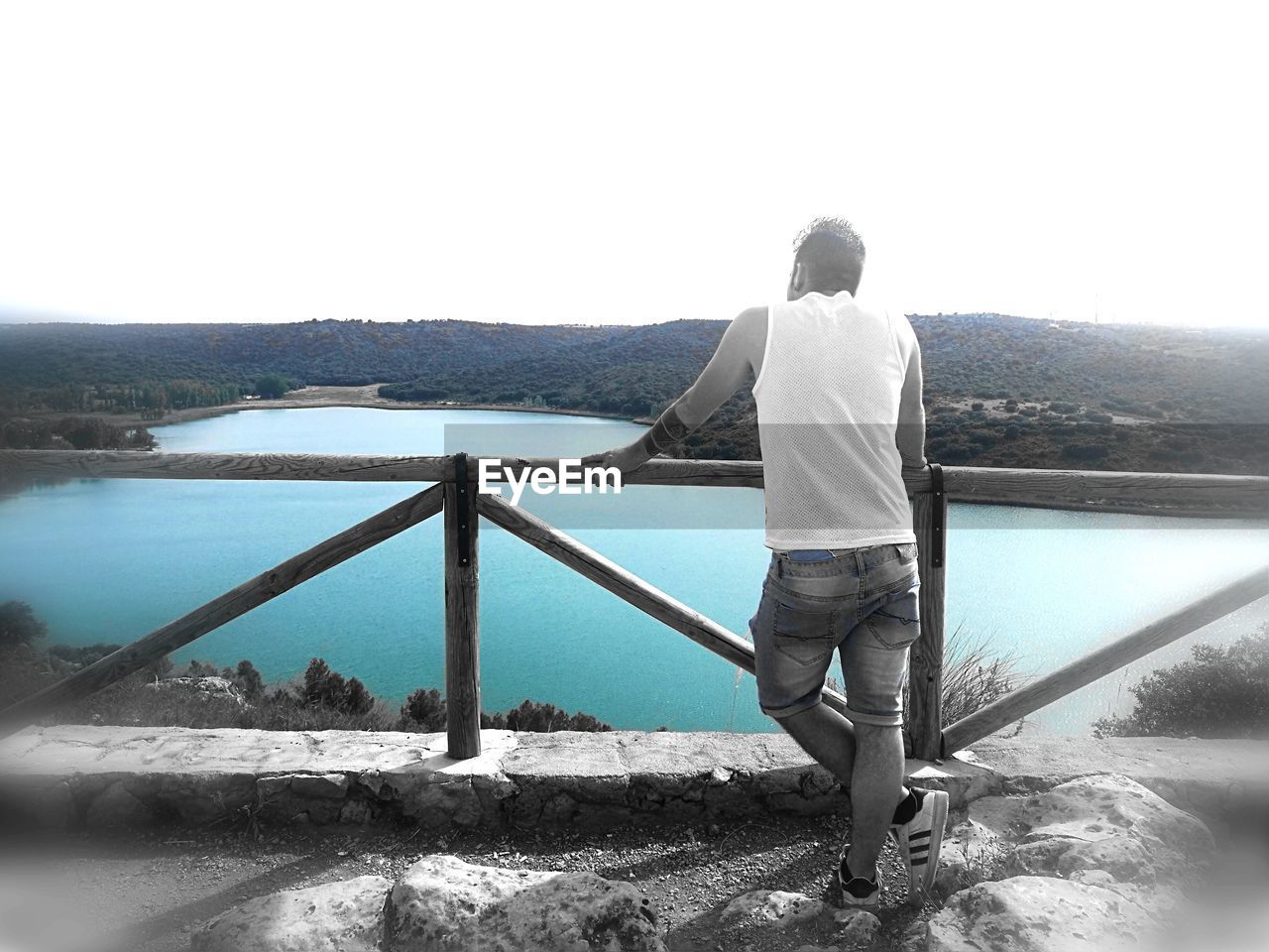 REAR VIEW OF MAN STANDING ON RETAINING WALL AGAINST SEA