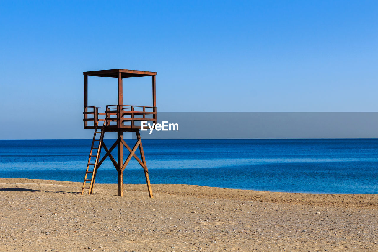 Wooden brown coastguard watchtower on the beach with blue sea in the background