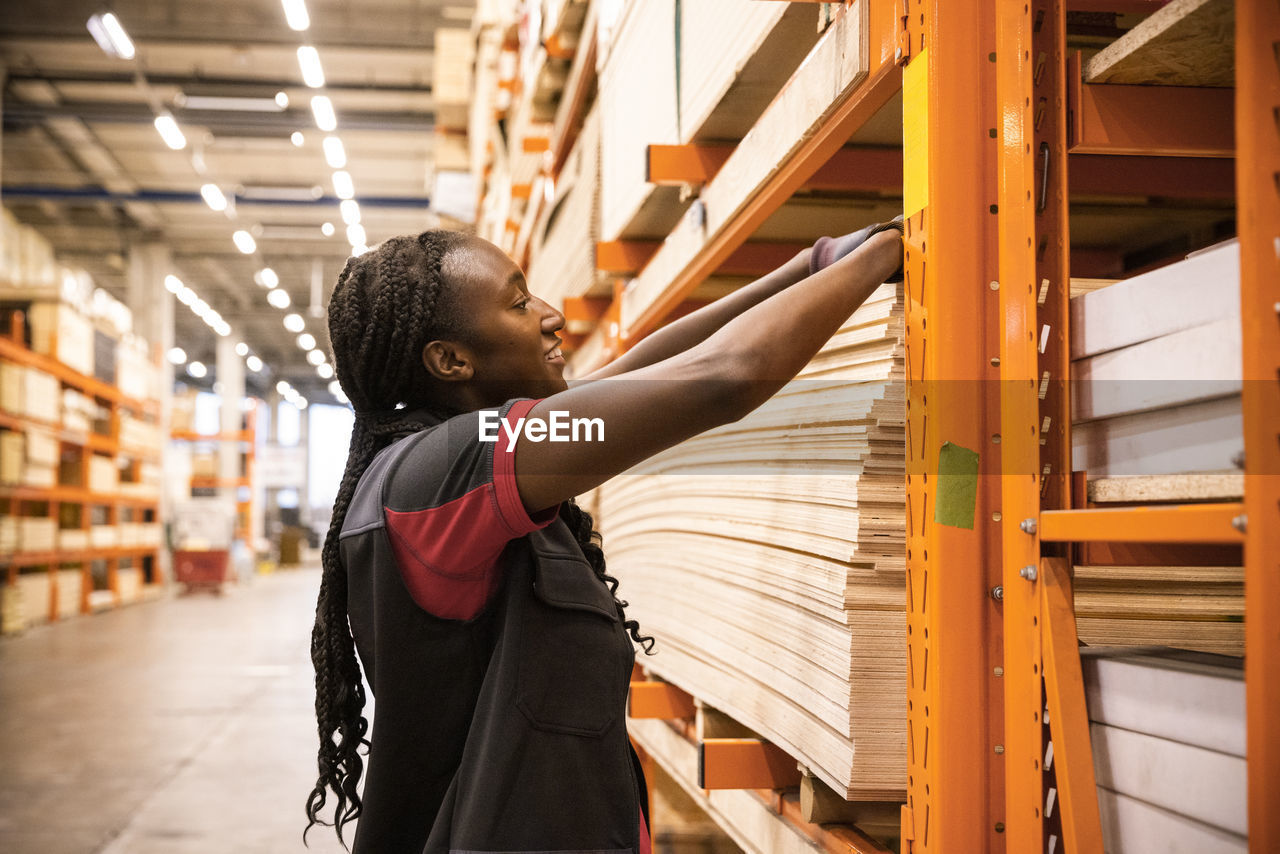 Smiling saleswoman arranging plywood in rack while working at hardware store