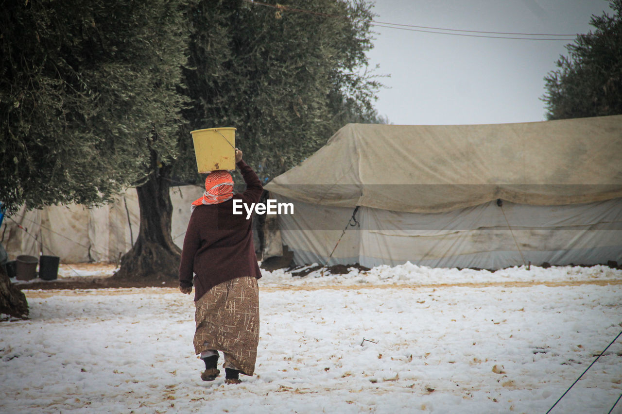 A refugee woman holds a bucket of water on her head during the snow in the camp.