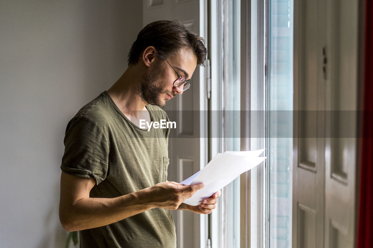 Male entrepreneur going through strategy while standing near window at office