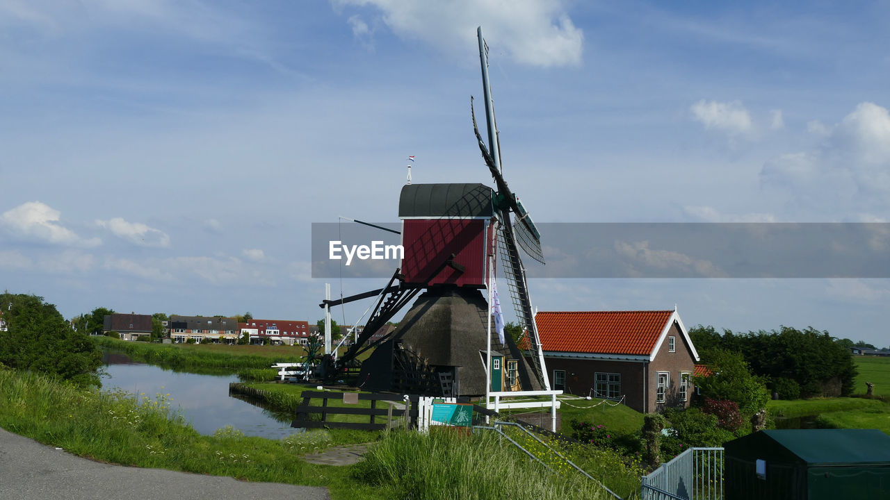 TRADITIONAL WINDMILL ON BUILDING BY PLANTS AGAINST SKY
