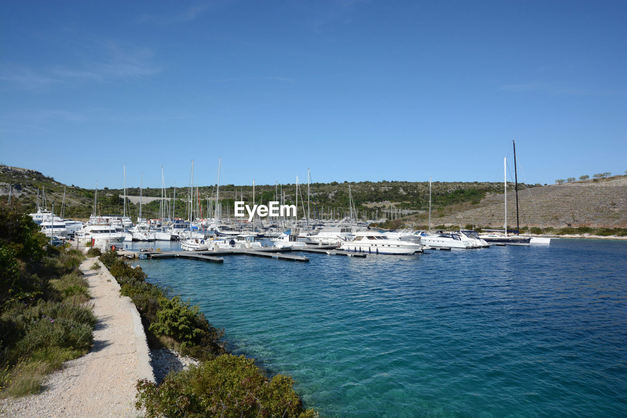 Sailboats moored in harbor on sea against blue sky