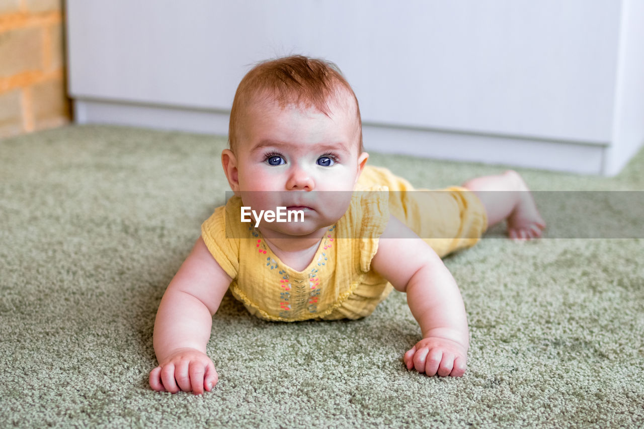 Portrait of little caucasian baby girl in yellow dress. child trying to crawl on a floor.