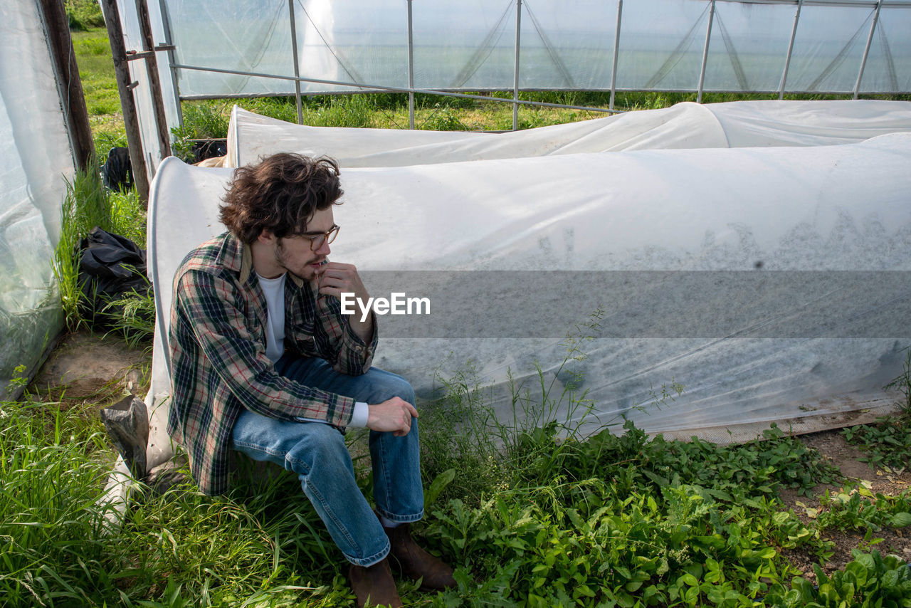 Young male farmer contemplates inside greenhouse by vegetable rows