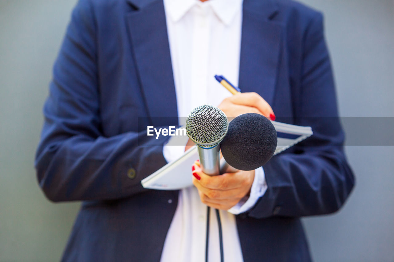 Female journalist at news conference or media event, writing notes, holding microphone