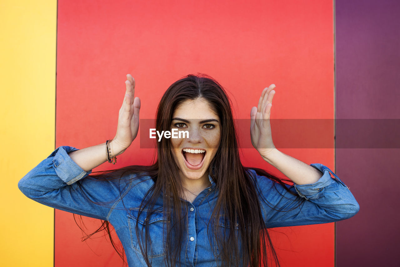 Portrait of screaming young woman in front of colourful wall