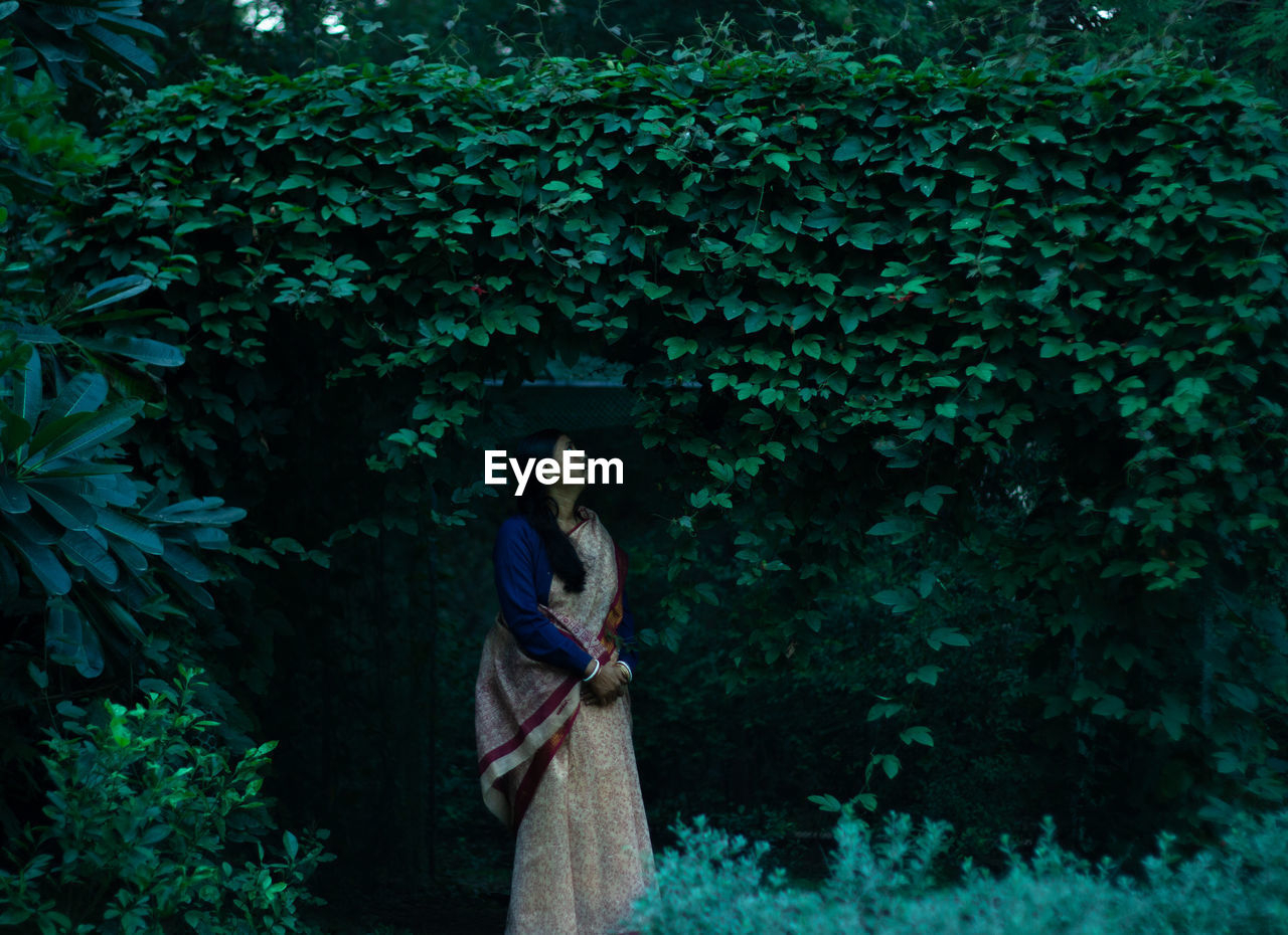 Woman in sari standing against plants